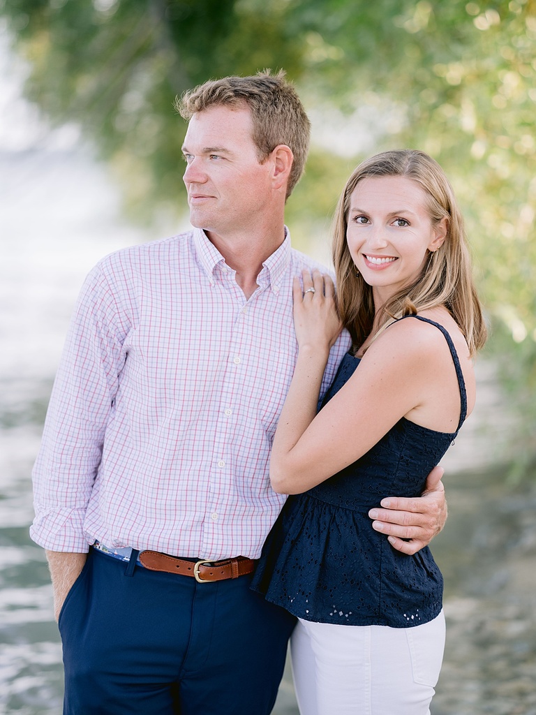 A woman cuddled up to her fiancé and smiling at the camera on a sunny summer evening