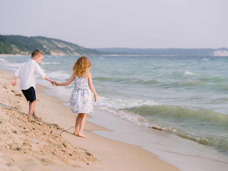 A boy and girl holding hands and playing on a sunny beach next to a Michigan lake