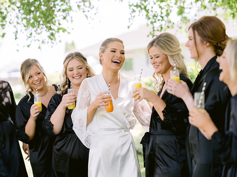 A bride on her wedding day drinking mimosas with her bridesmaids and laughing