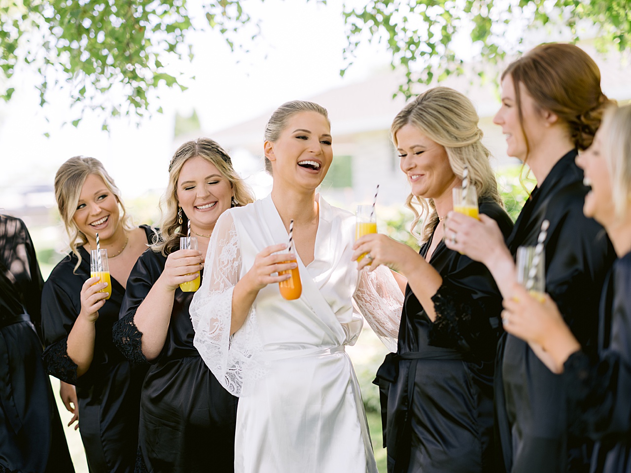 A bride on her wedding day drinking mimosas with her bridesmaids and laughing