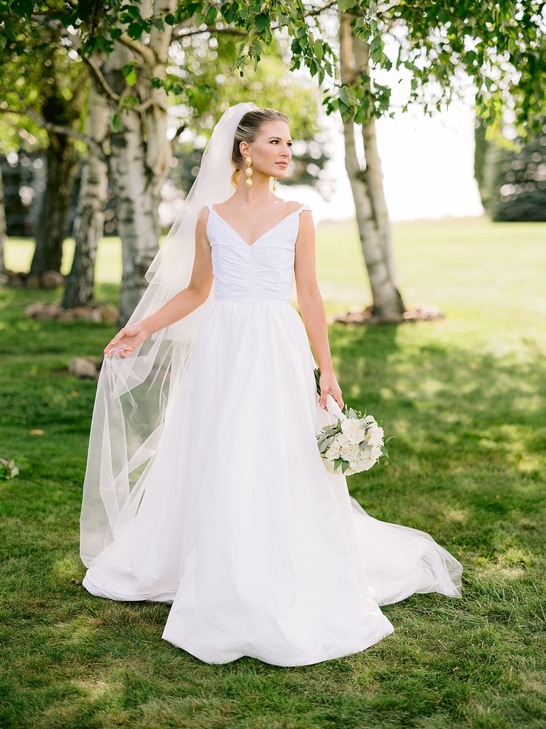 A bride taking portraits on a sunny day and holding her long veil to the side