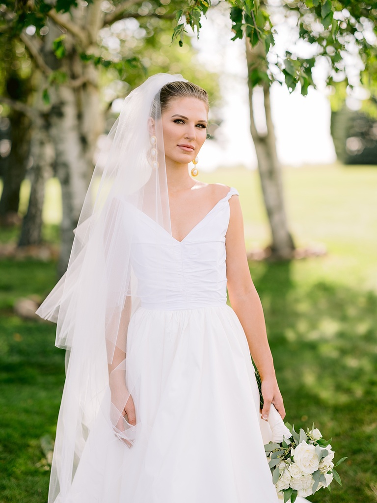 A bride taking portraits on a county estate with green grass and birch trees