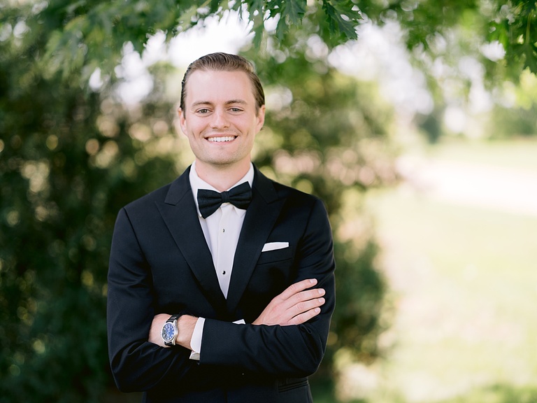 A groom smiling with his arms crossed on his wedding day