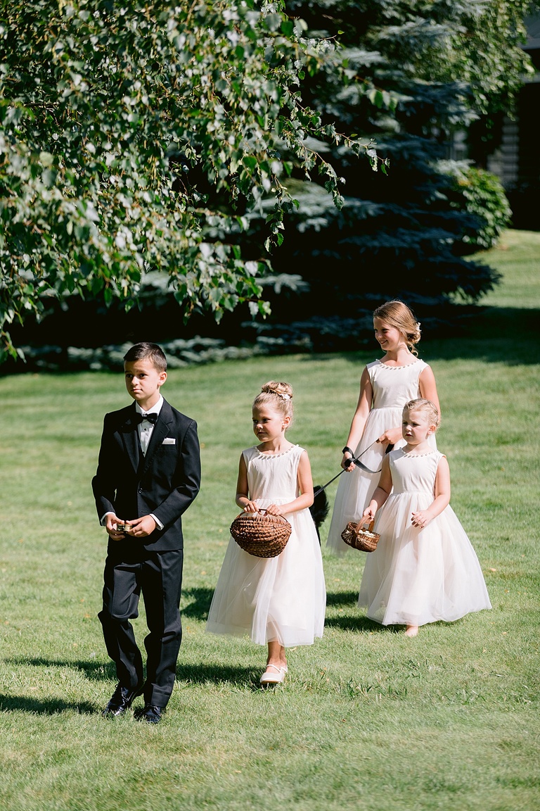 The flower girls, ring bearer, and small black dog walking dow the aisle