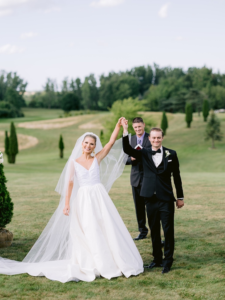 A bride and groom raising their hands together at their guests after sharing their first kiss