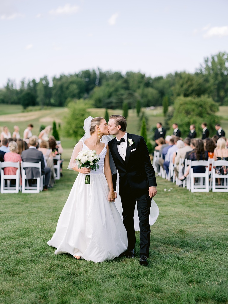 A bride and groom kissing white holding hands with their guests seated at the ceremony in the background