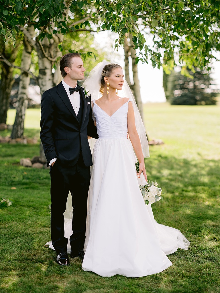 A bride in a white dress and long veil and groom in a black tux taking wedding portraits
