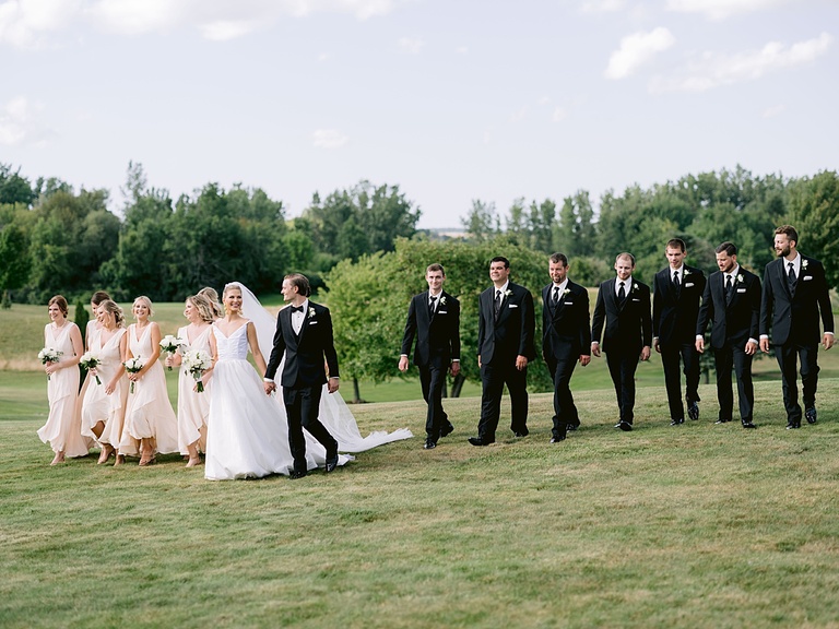 A wedding party walking together in a grassy field