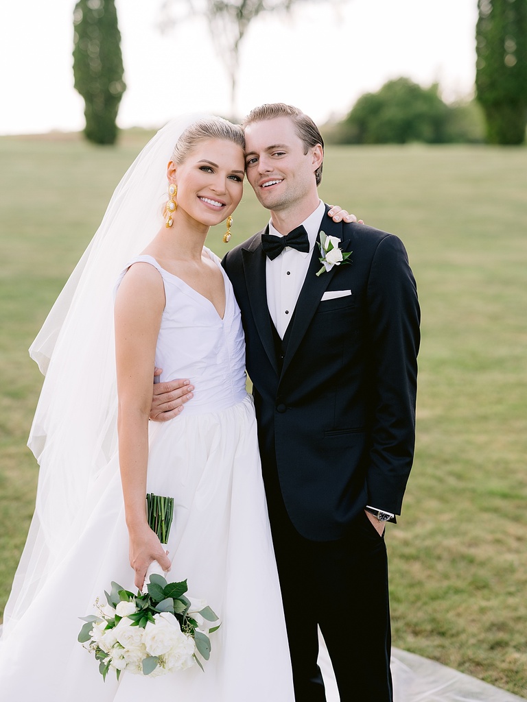 A bride and groom resting theirs heads on each other and smiling at the camera