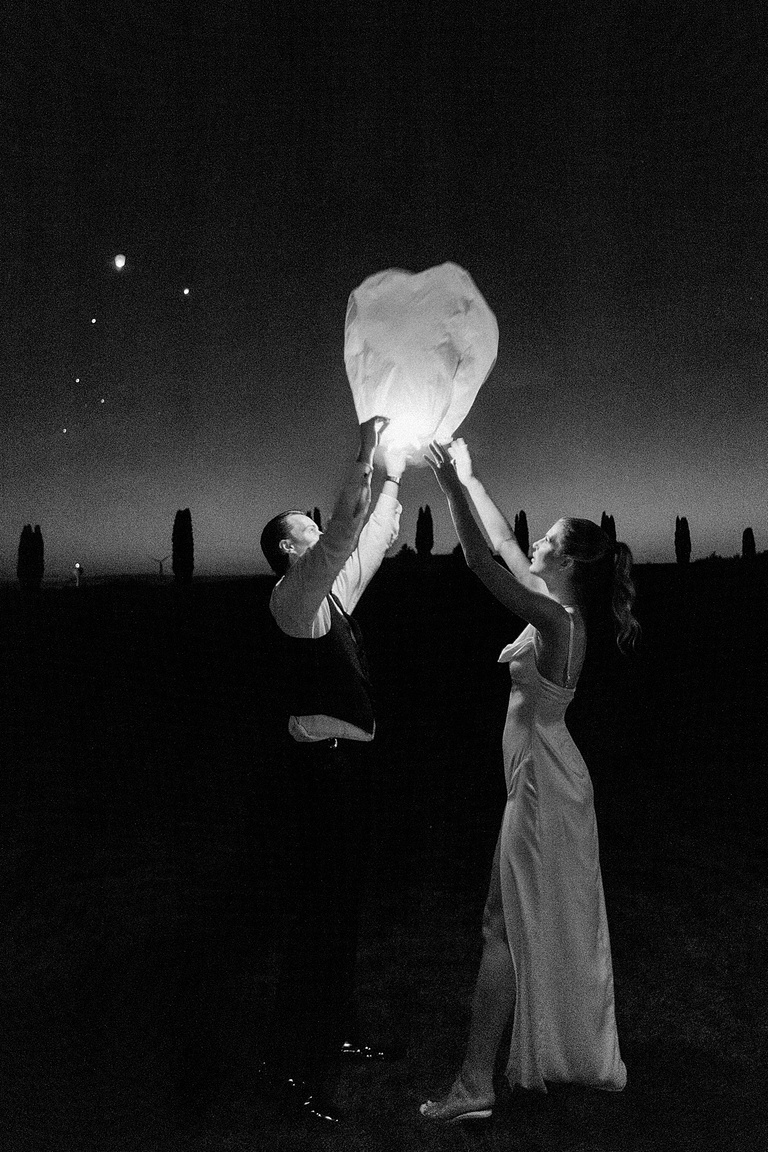 A bride and groom letting go of a lantern at dusk on their wedding day
