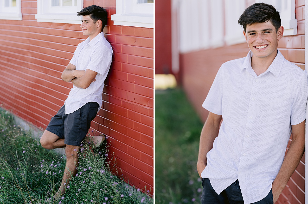 A young man leans against a a red building in Northern Michigan for senior portraits