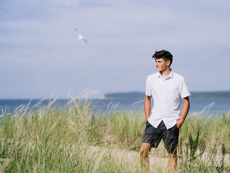 A high school senior stands in the tall grass of a beach near Lake Michigan