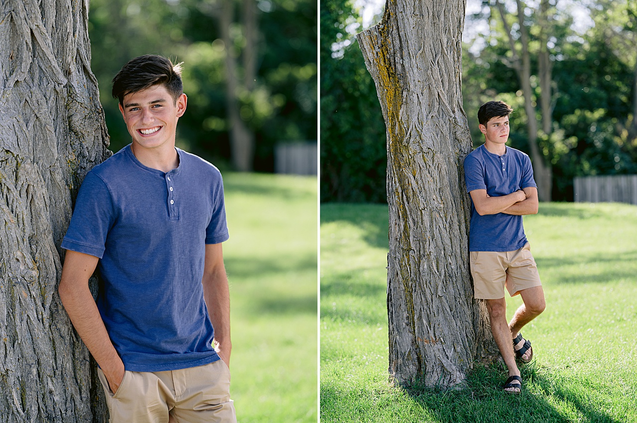 A senior boy leans against a tree for senior photos while wearing a blue shirt