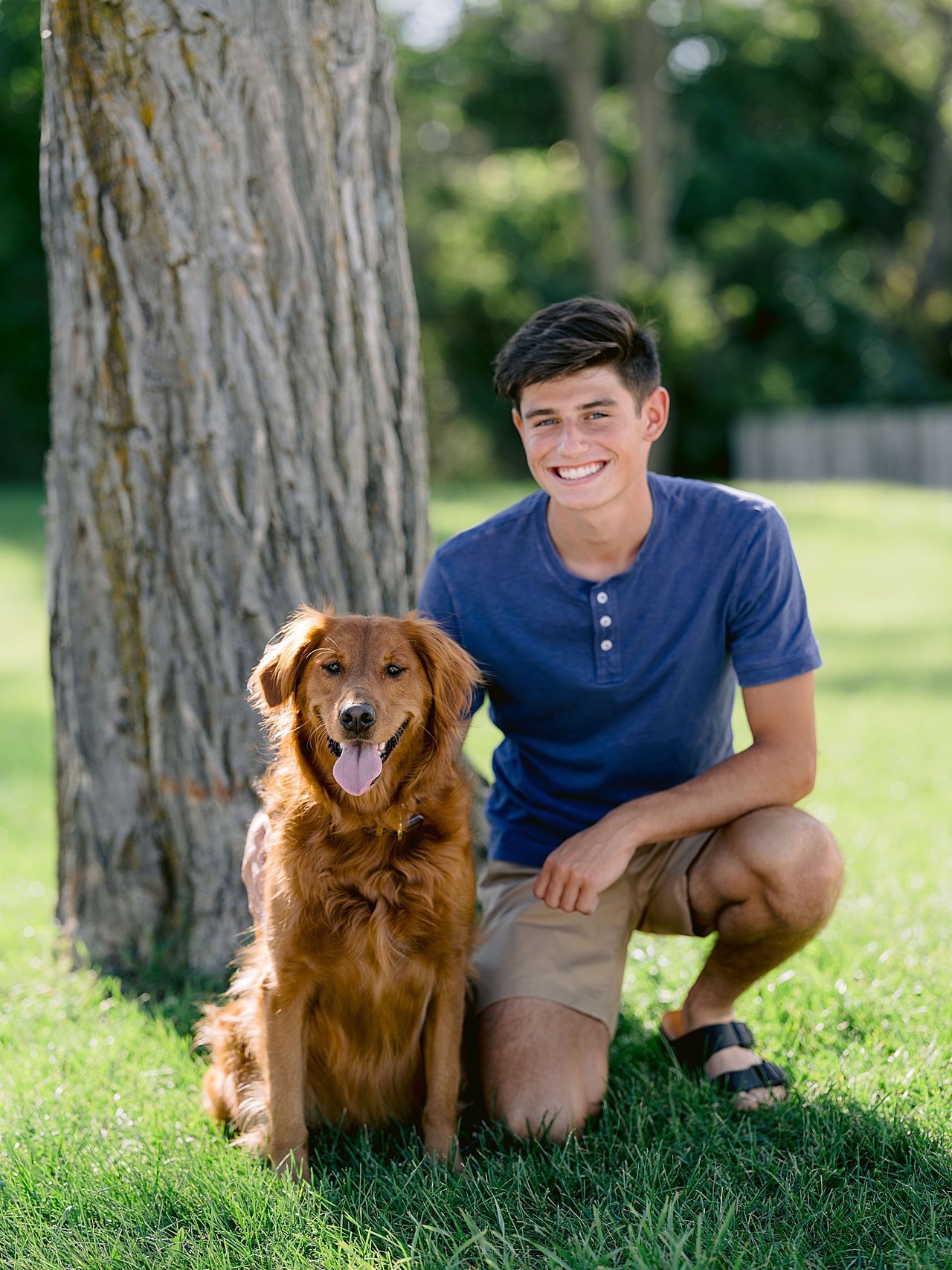 A boy takes a knee with his arm around his golden retriever and smiles in Northern Michigan