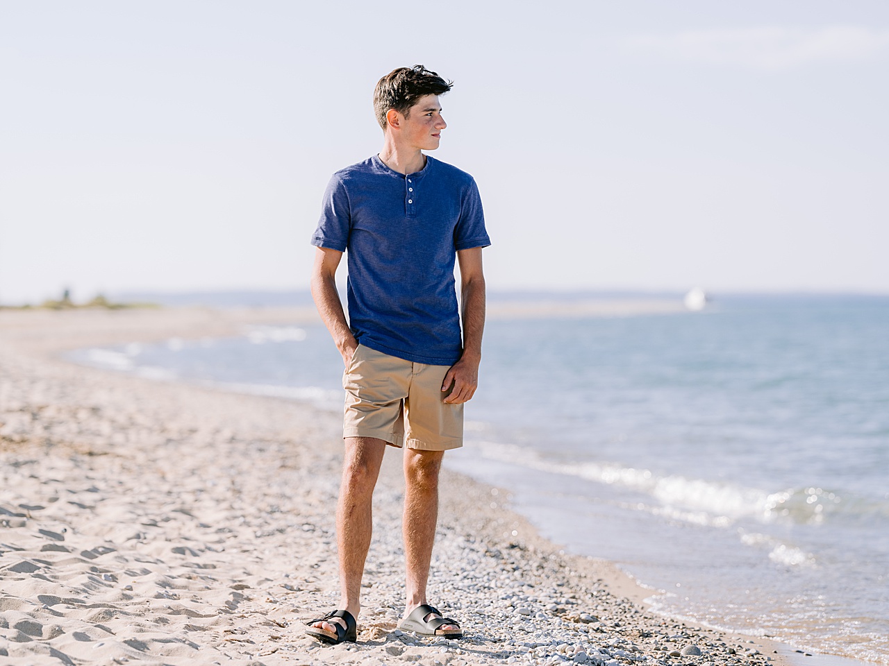 A boy in a blue shirt stands with a hand in his pocket and looks out over Lake Michigan