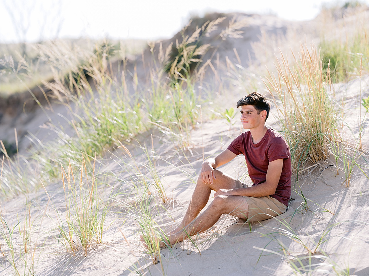 A boy looks off in the distance while sitting on a sandy hill in Northern Michigan