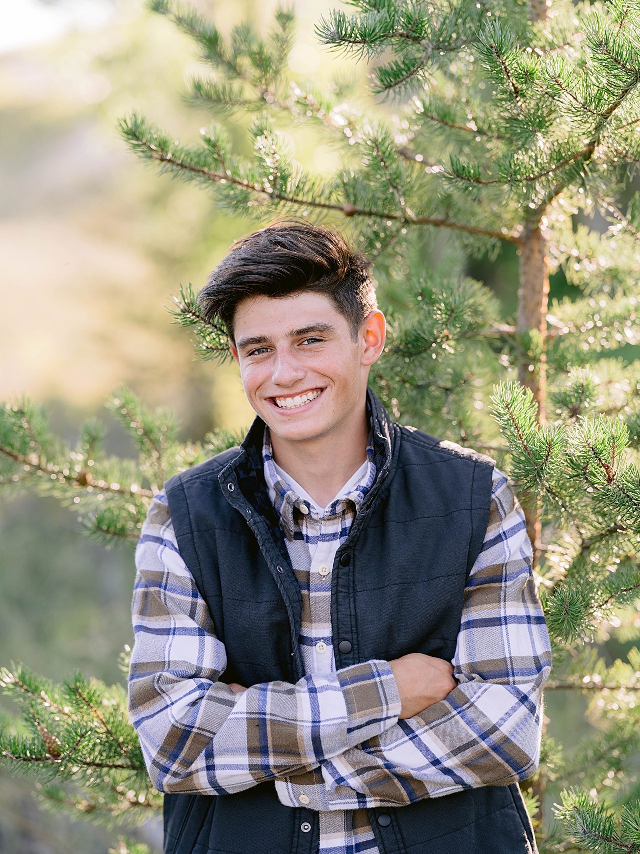 A male poses for Glen Arbor senior portrait photography on a sunny day near a pine tree
