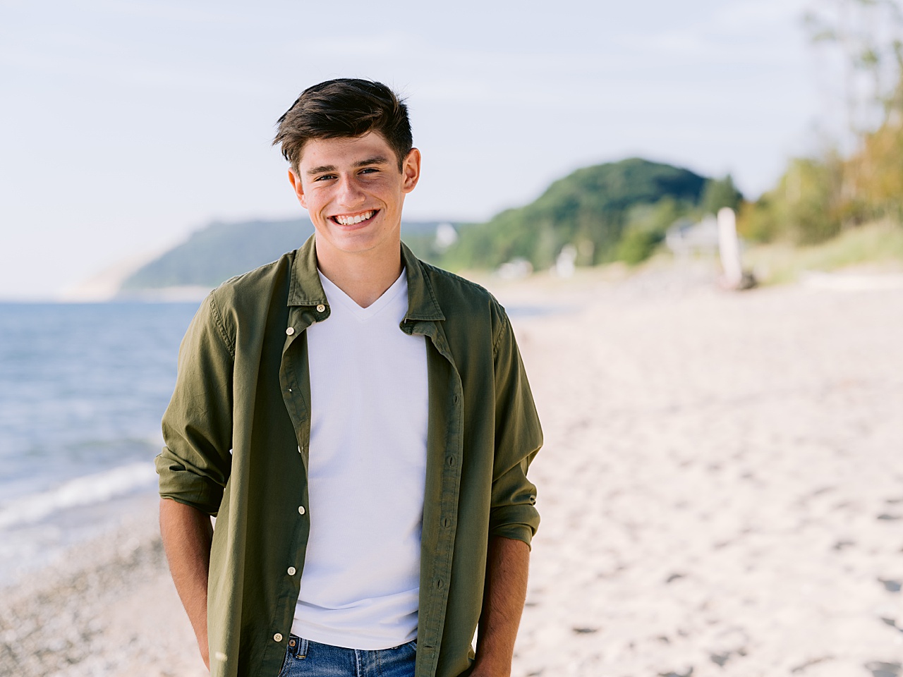 A young man poses for senior portraits with sandy dunes in the background