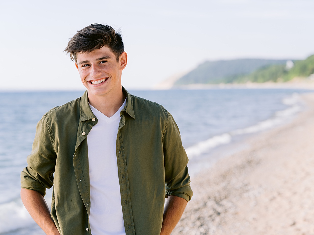 A boy smiles for senior photos in Northern Michigan with a lake behind him
