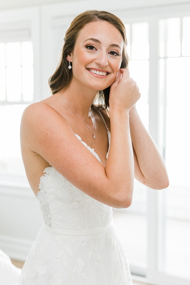 A bride putting on her small dangling earrings on her wedding day