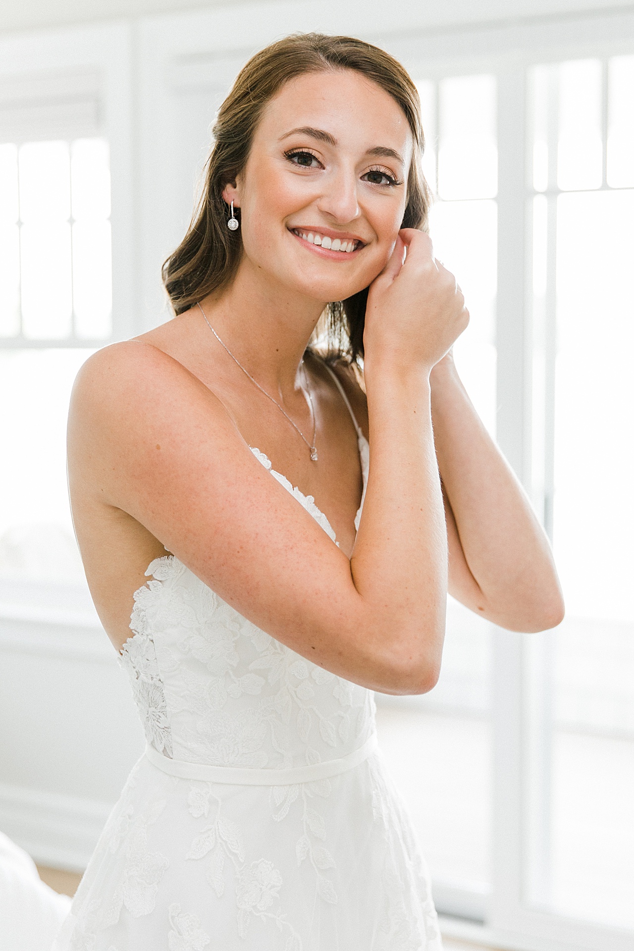 A bride putting on her small dangling earrings on her wedding day