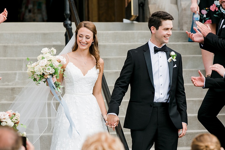 A bride and groom smiling at their guests as they exit the catholic church