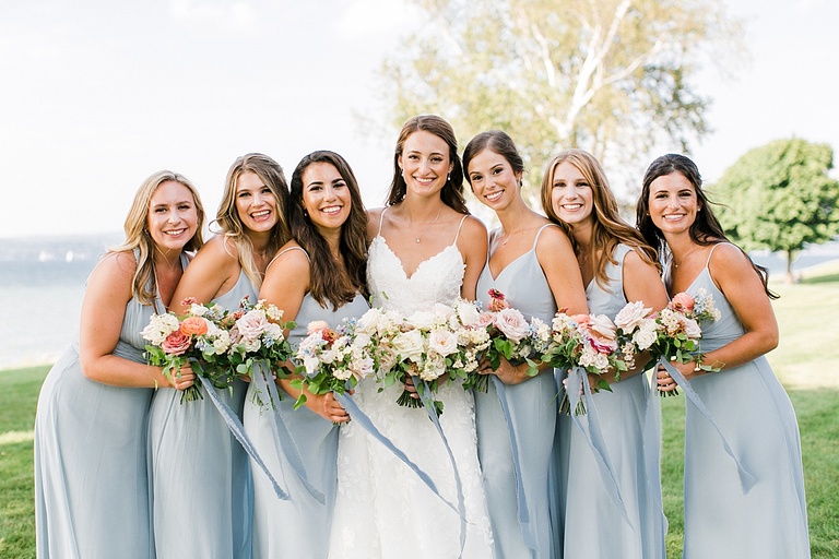 A bride and her bridesmaids close together smiling at the camera on a sunny day by the lake in Northern Michigan