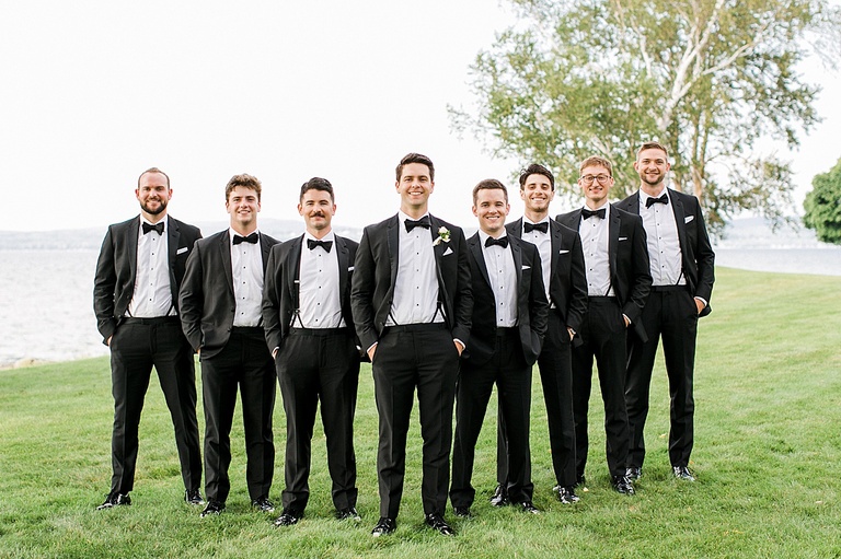 A groom and his groomsmen in black tuxes taking portraits by the lake