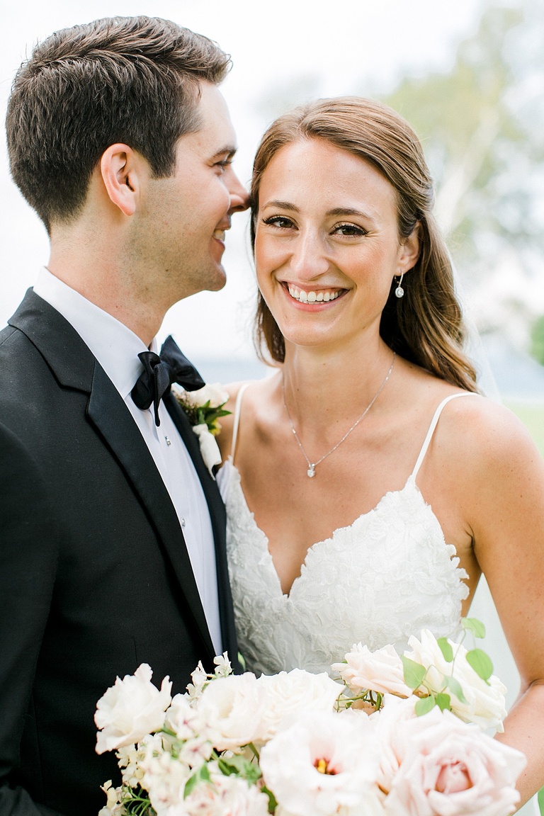 A bride smiling as her groom whispers in her ear