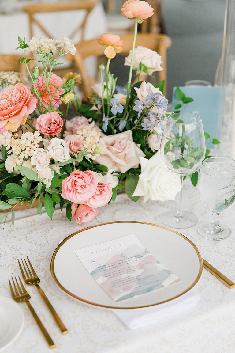 A white place with a gold rim on a La Tavola linen with colorful pastel florals by BLOOM floral design