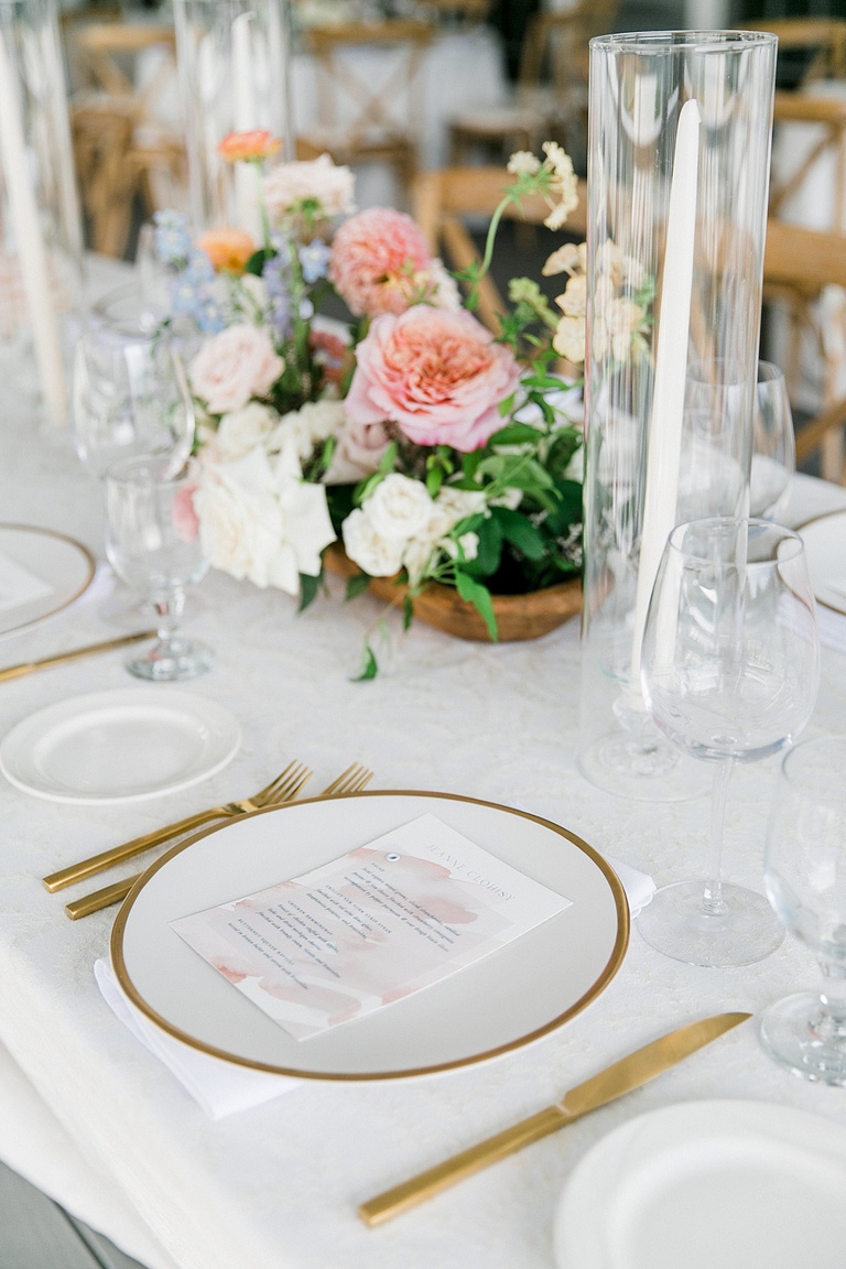 A reception dinner plate with gold silverware and a pastel paper menu