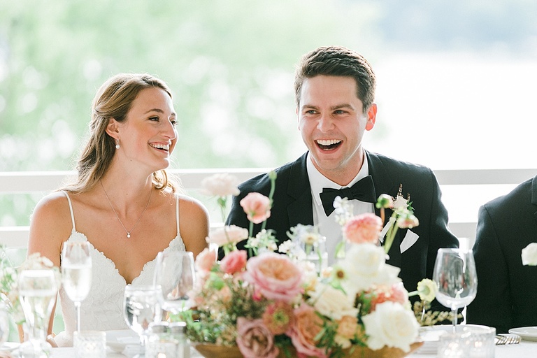 A bride and groom laughing during speeches and toasts on the porch of the Walloon Lake Country Club