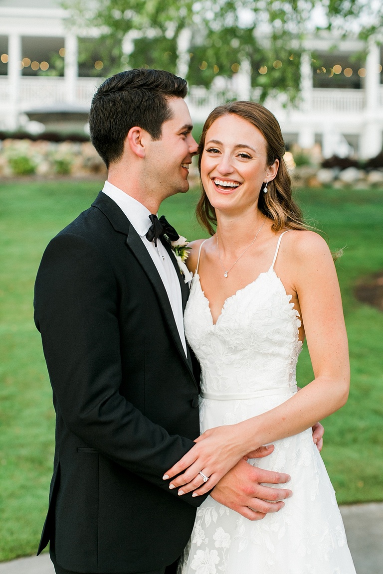 A bride laughing at the camera while the groom whispers in her ear