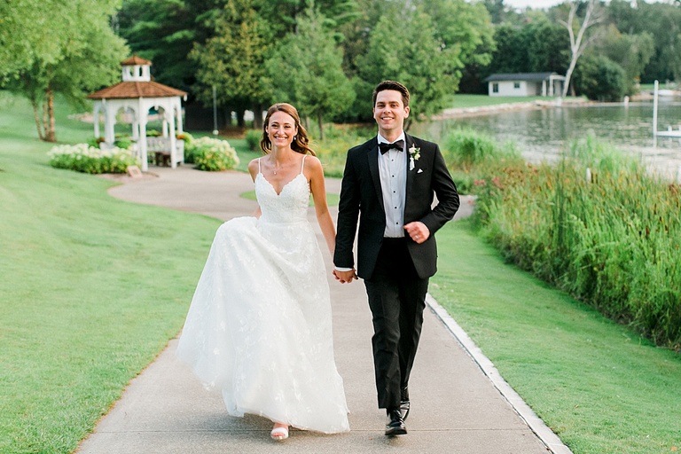 A bride and groom holding hands and running together back to their wedding reception at the Walloon Lake Country Club