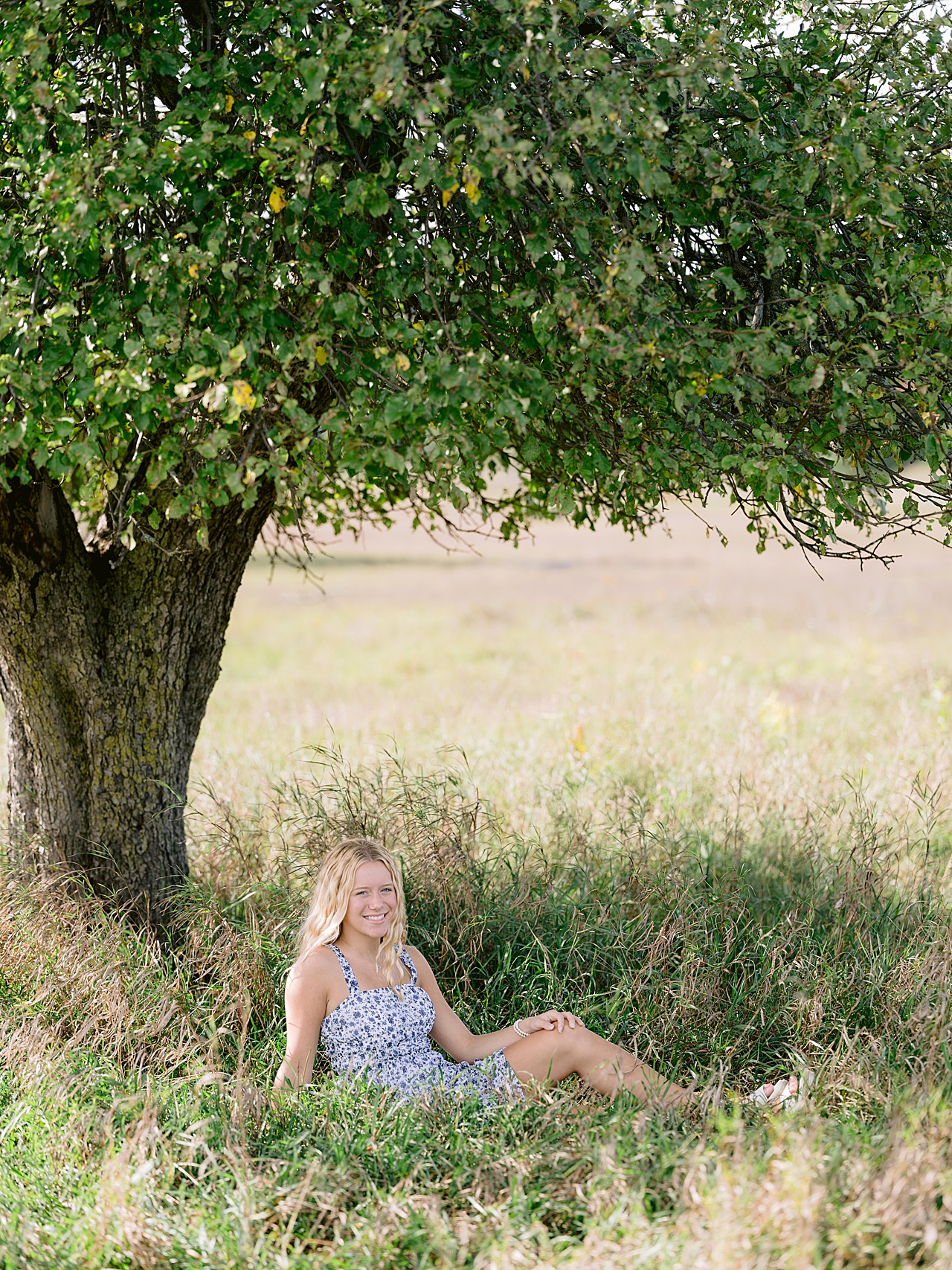A photo of a girl laying down and smiling in tall grass in sunny Michigan