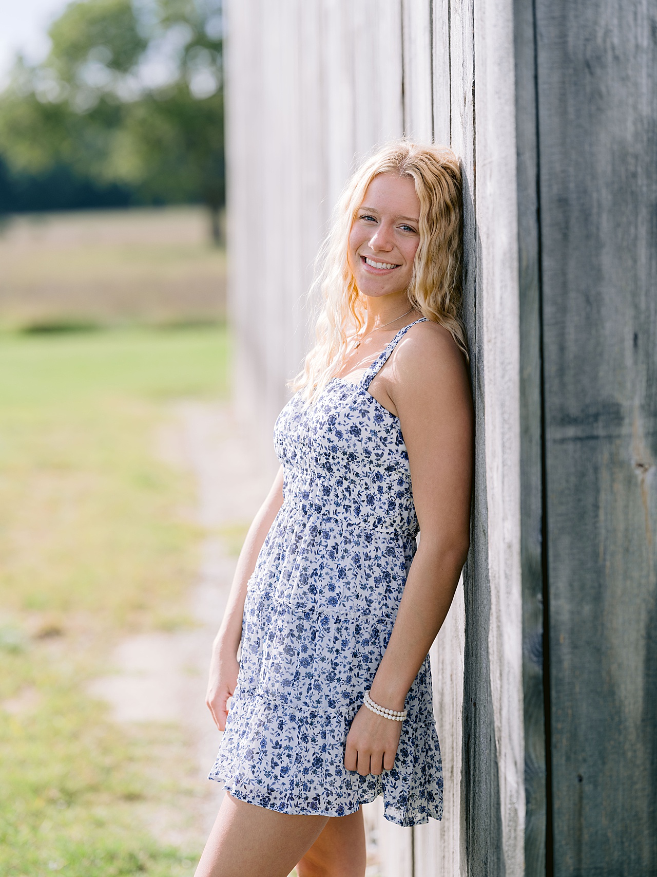 A girl in a floral summer dress leans against a barn in Oneida, Michigan