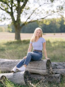 A girl sits on old logs on a sunny day with trees in the background