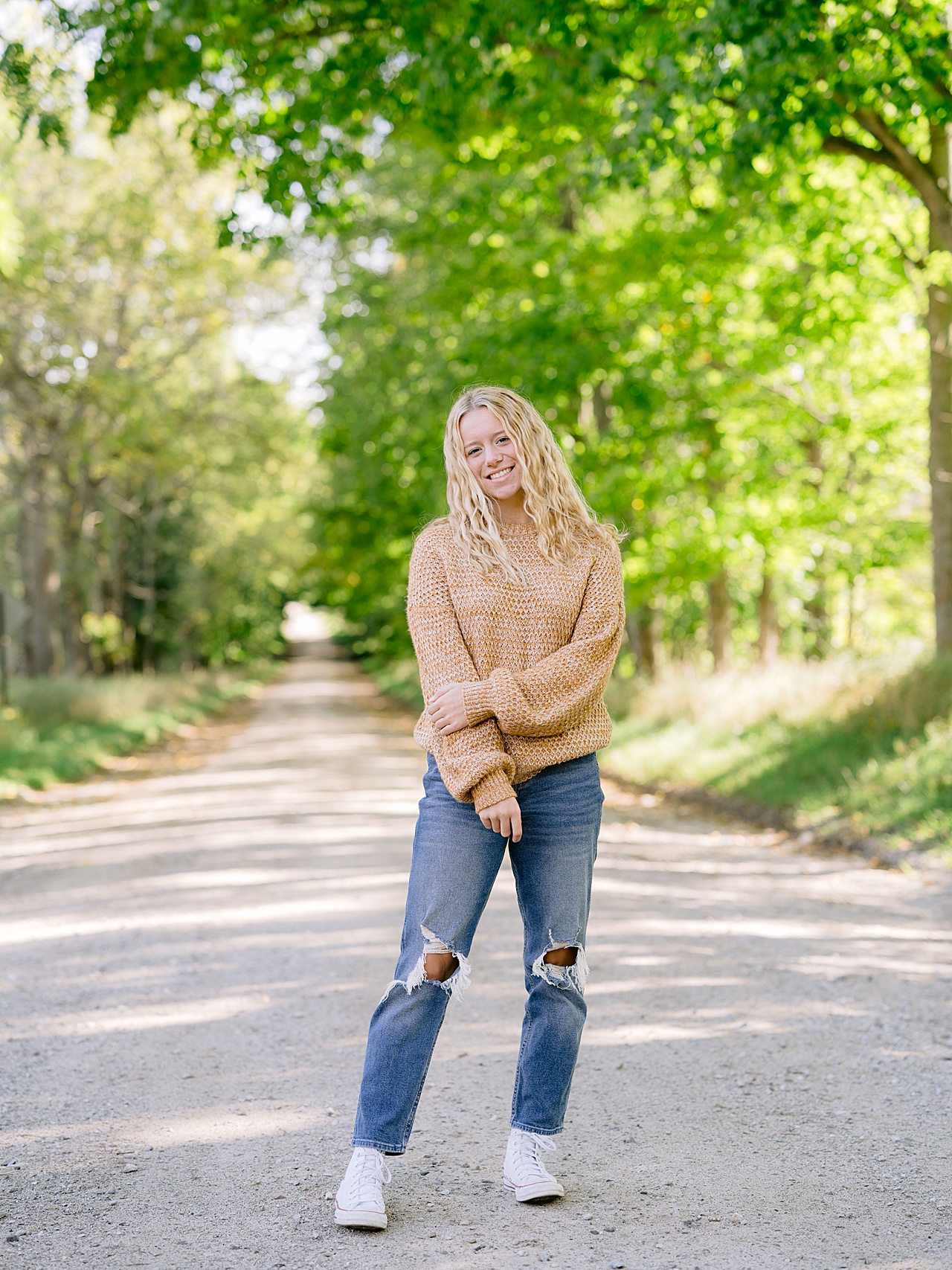 A high school girl stands smiling on a country road in Michigan