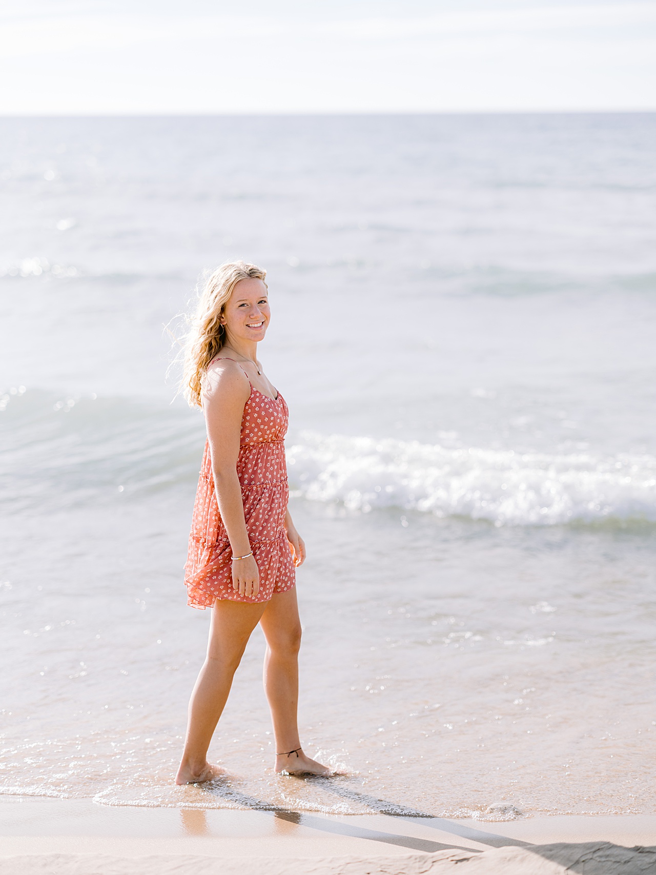 A girl in a dress smiles while walking in the water of Lake Michigan in the summer