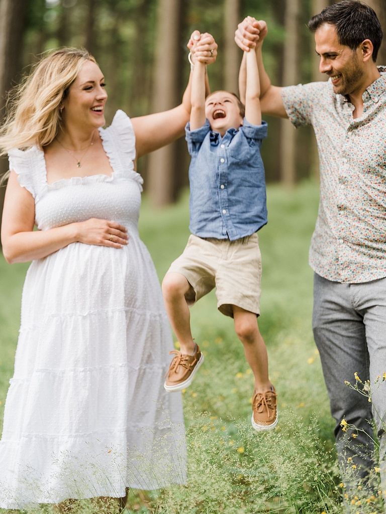 A mother and father holding their sons hands lift him laughing off the ground in Michigan