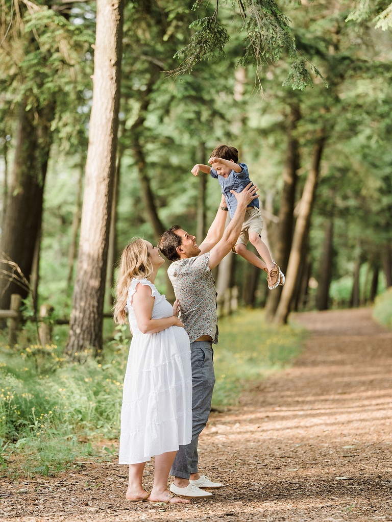 A man and woman throw their son into the air while smiling in the woods of Northern Michigan