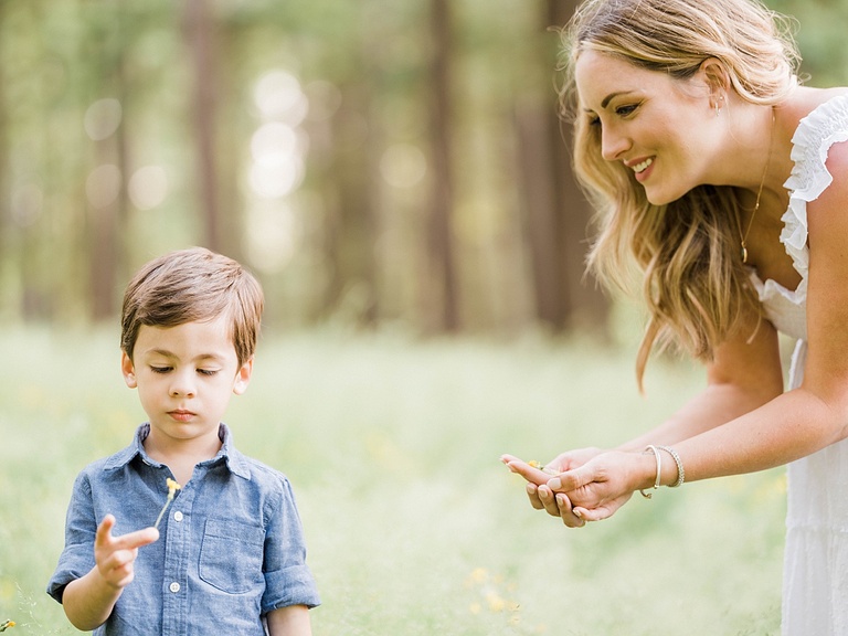 A little boy looks at a flower while his mother smiles at him with cupped hands in Michigan