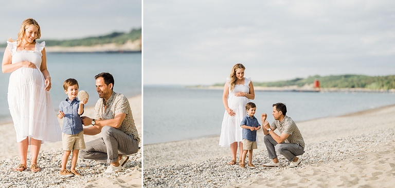 An expectant family of three stand on the beach smiling and looking at rocks