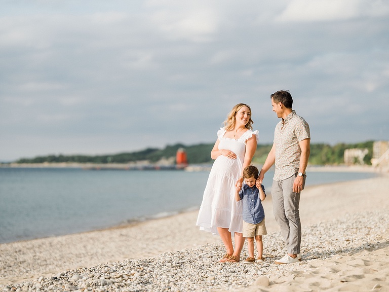A mother and father stand holding their sons hands on a beach with Lake Charlevoix beside them