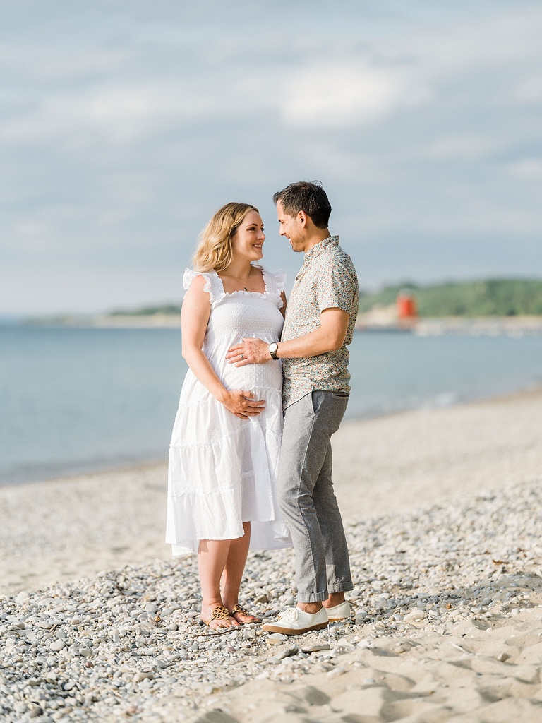 A man and pregnant woman look into each other's eyes and smile while holding her belly