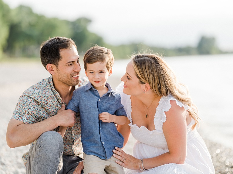 A man and woman both look at a young boy and smile at him with their arms around him