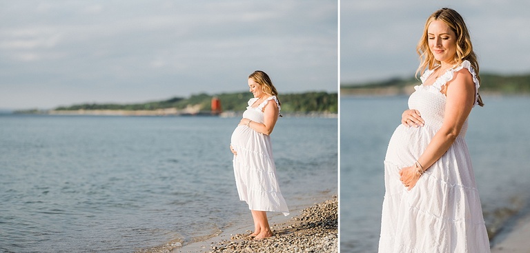 An expectant mother wearing a white dress holds her belly and smiles in Northern Michigan