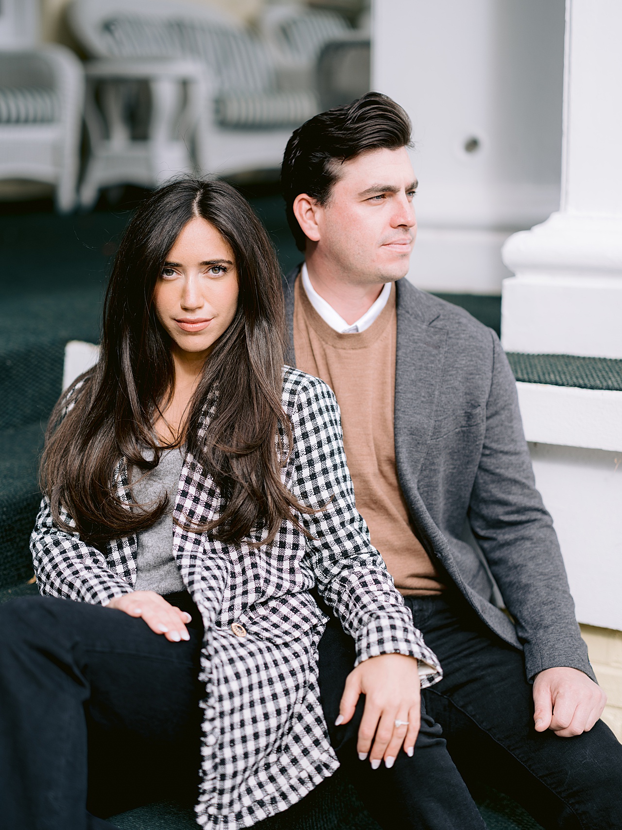 A woman in a checkered jacket leans agains a man in a blazer in front of The Perry