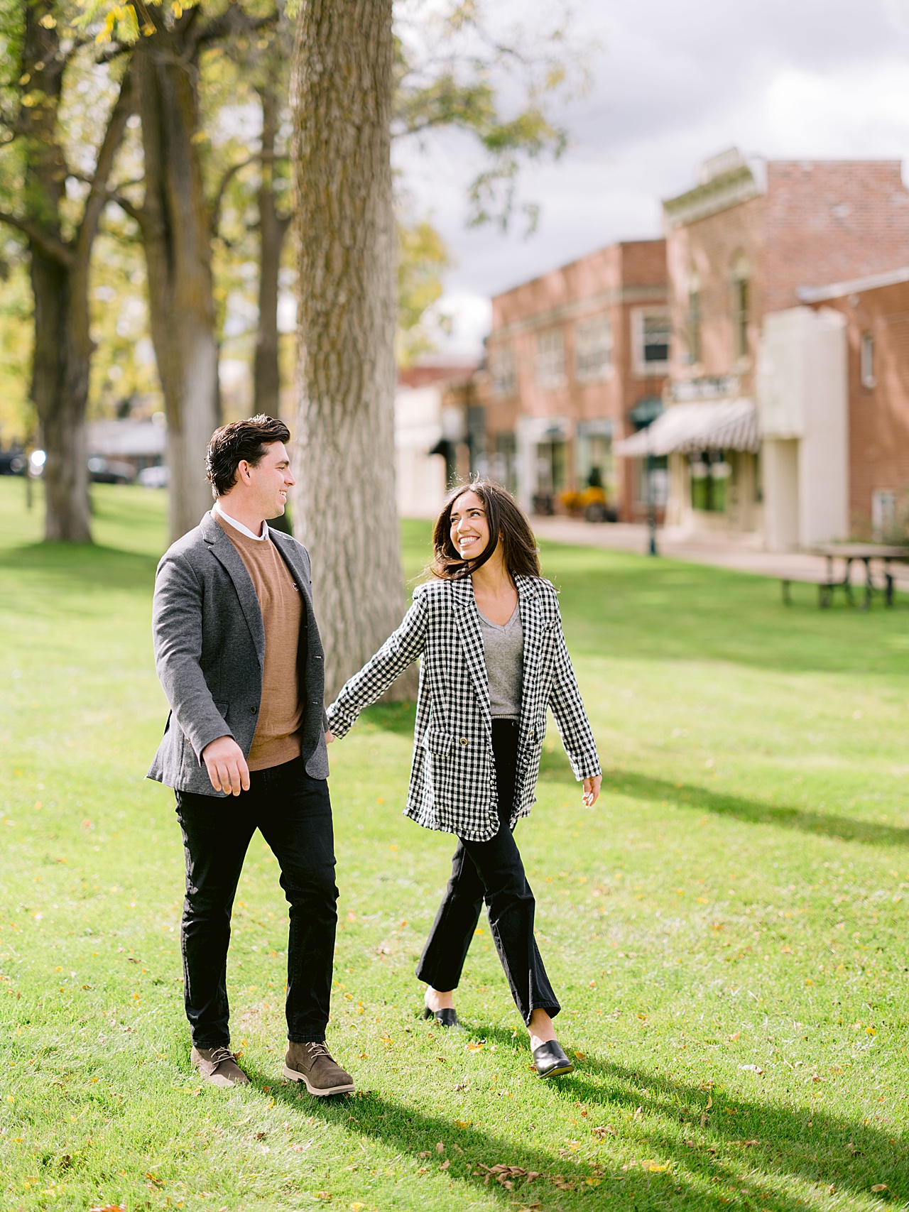 A man and woman walk through a downtown park while smiling at each other