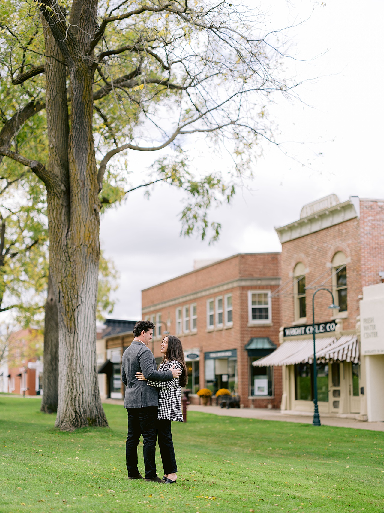 An engaged couple poses in front of a large walnut tree in a downtown area